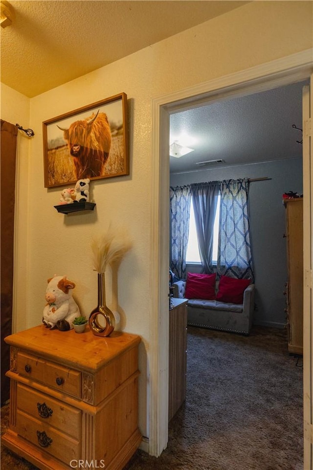 hall featuring a textured ceiling and dark carpet