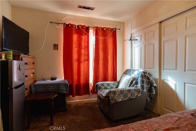 bedroom with a closet, dark colored carpet, and stainless steel refrigerator