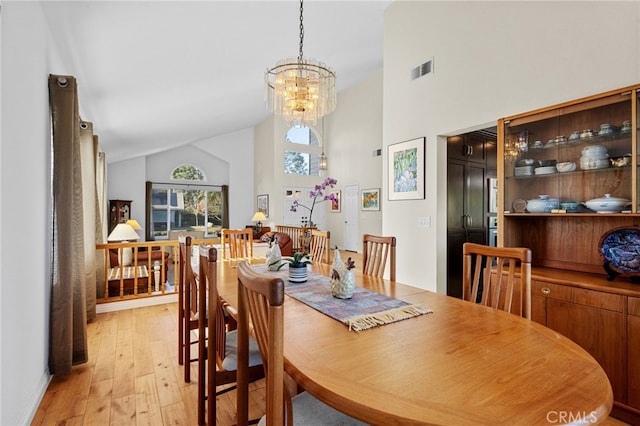 dining room featuring high vaulted ceiling, a chandelier, and light wood-type flooring