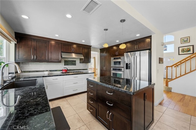 kitchen with a kitchen island, appliances with stainless steel finishes, decorative light fixtures, sink, and dark stone counters