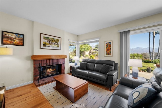 living room featuring a mountain view, a healthy amount of sunlight, light hardwood / wood-style floors, and a brick fireplace