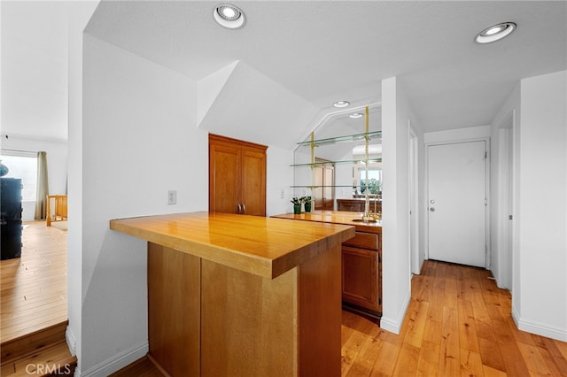 kitchen featuring vaulted ceiling, butcher block counters, sink, kitchen peninsula, and light wood-type flooring