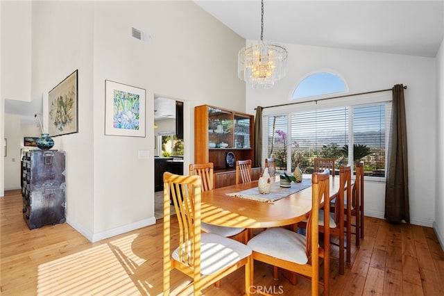 dining area with high vaulted ceiling, a chandelier, and light hardwood / wood-style flooring