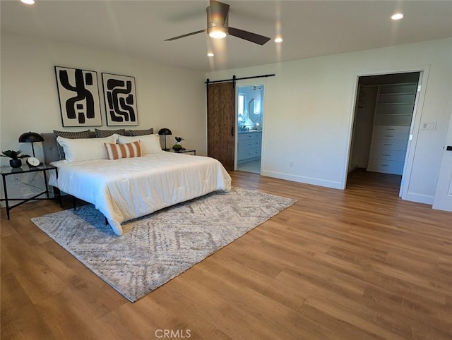 bedroom featuring a spacious closet, a barn door, ceiling fan, a closet, and wood-type flooring