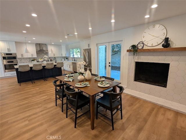 dining room featuring french doors, a fireplace, sink, and light hardwood / wood-style flooring