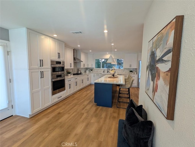 kitchen featuring pendant lighting, a center island, wall chimney exhaust hood, white cabinetry, and tasteful backsplash