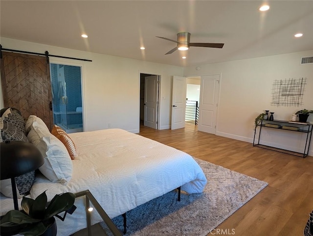 bedroom with ceiling fan, hardwood / wood-style floors, a barn door, and connected bathroom