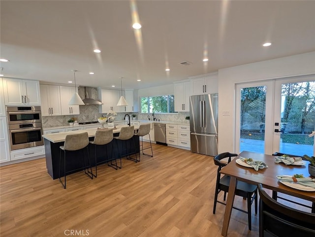 kitchen with stainless steel appliances, decorative light fixtures, light wood-type flooring, a kitchen island, and wall chimney exhaust hood