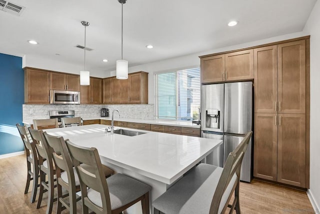 kitchen with pendant lighting, appliances with stainless steel finishes, an island with sink, light hardwood / wood-style floors, and sink