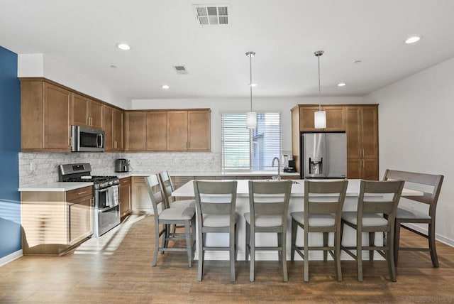 kitchen with decorative light fixtures, backsplash, a breakfast bar, a kitchen island with sink, and stainless steel appliances