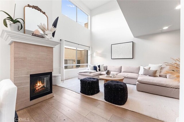 living room with wood-type flooring, a tiled fireplace, and a towering ceiling