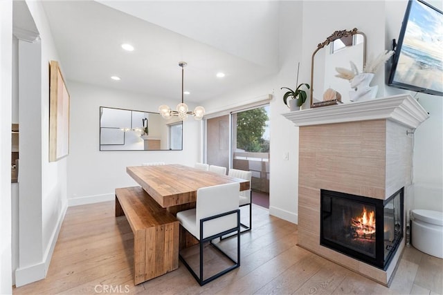 dining space with a multi sided fireplace, an inviting chandelier, and light hardwood / wood-style floors