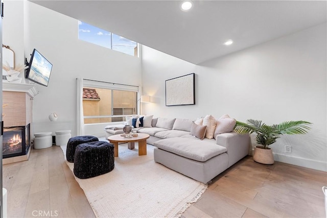 living room featuring light hardwood / wood-style floors, a high ceiling, and a tile fireplace