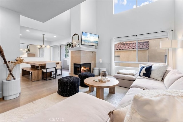 living room featuring a towering ceiling, light hardwood / wood-style flooring, a tiled fireplace, and a notable chandelier