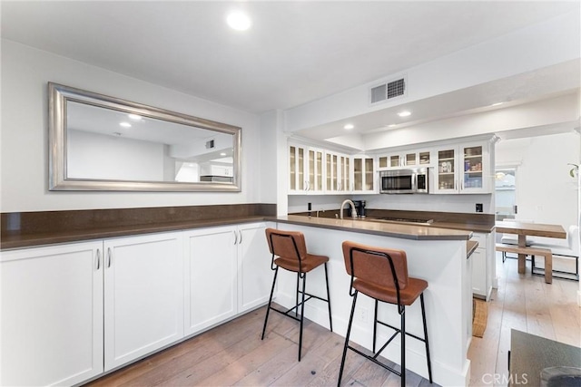 kitchen with light hardwood / wood-style flooring, white cabinetry, kitchen peninsula, and a kitchen breakfast bar