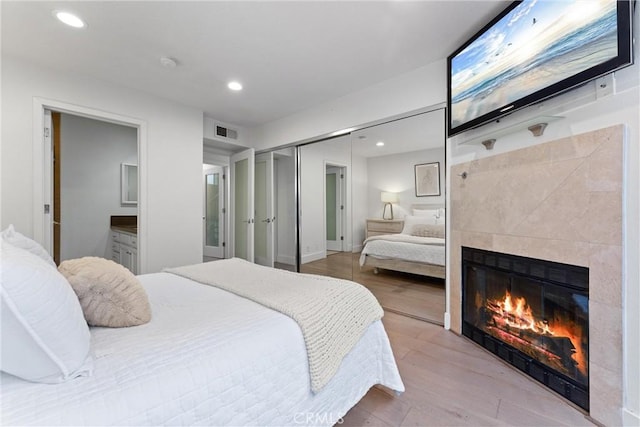 bedroom with a tiled fireplace, light wood-type flooring, a closet, and ensuite bathroom