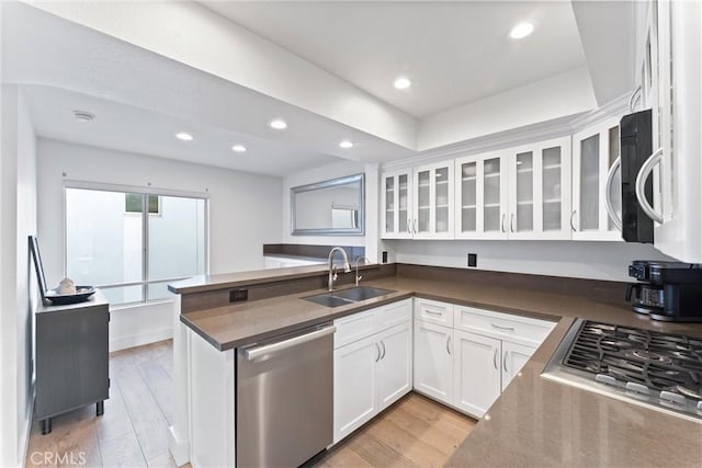 kitchen featuring appliances with stainless steel finishes, white cabinetry, sink, light wood-type flooring, and kitchen peninsula