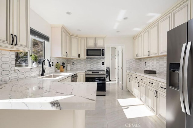 kitchen featuring kitchen peninsula, sink, stainless steel appliances, cream cabinetry, and light stone counters