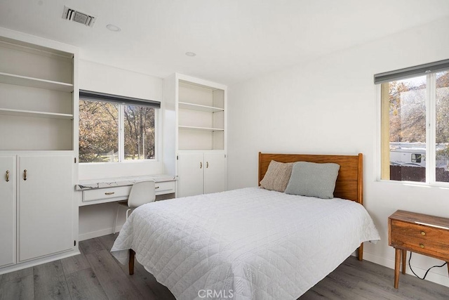 bedroom featuring dark wood-type flooring, multiple windows, and built in desk