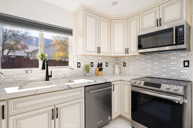 kitchen featuring stainless steel appliances, tasteful backsplash, light stone counters, cream cabinets, and sink