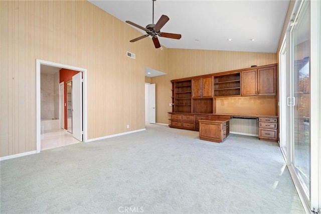 unfurnished living room featuring light carpet, ceiling fan, built in desk, and high vaulted ceiling