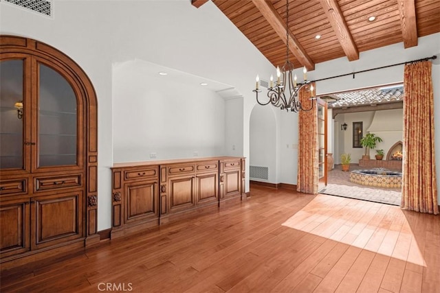 unfurnished dining area featuring an inviting chandelier, hardwood / wood-style flooring, wooden ceiling, high vaulted ceiling, and beam ceiling