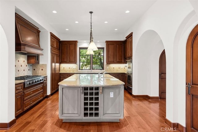 kitchen featuring hardwood / wood-style floors, pendant lighting, a center island with sink, light stone countertops, and appliances with stainless steel finishes