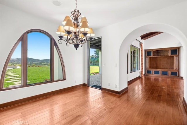 unfurnished dining area with vaulted ceiling with beams, an inviting chandelier, a mountain view, and hardwood / wood-style floors