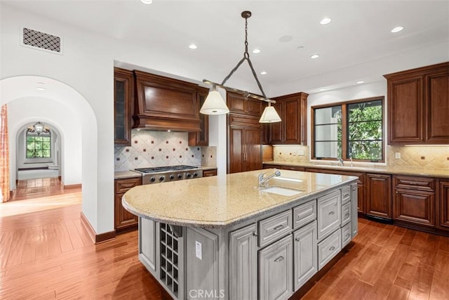 kitchen featuring stainless steel gas stovetop, sink, hanging light fixtures, an island with sink, and light stone counters