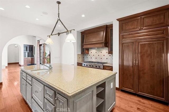 kitchen with decorative backsplash, sink, stainless steel gas cooktop, a kitchen island with sink, and light stone counters