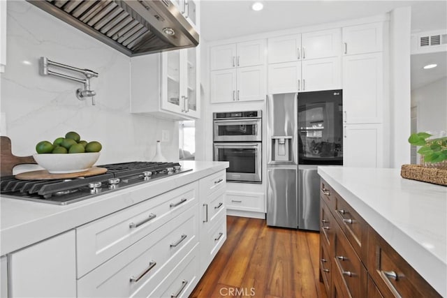 kitchen featuring white cabinets, wall chimney exhaust hood, dark hardwood / wood-style flooring, stainless steel appliances, and light stone counters