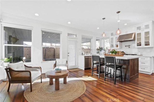 kitchen featuring white cabinets, a kitchen island, a kitchen bar, hanging light fixtures, and stainless steel dishwasher