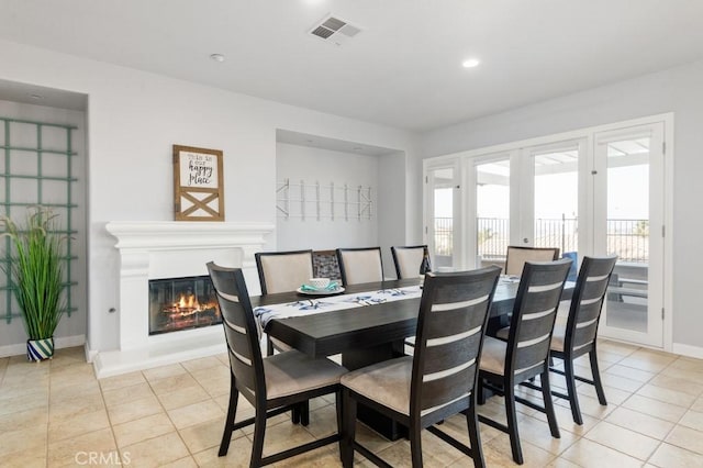 dining area featuring french doors, visible vents, a glass covered fireplace, light tile patterned flooring, and baseboards