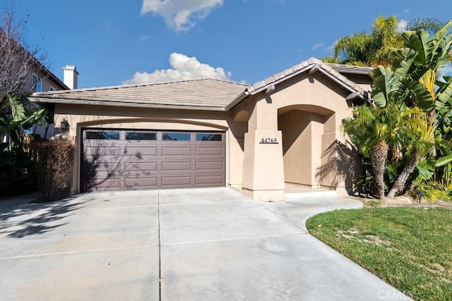 single story home with concrete driveway, an attached garage, a tiled roof, and stucco siding