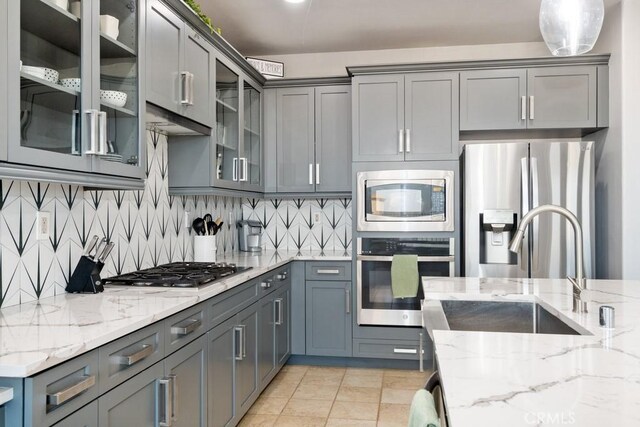 kitchen with stainless steel appliances, decorative backsplash, light stone countertops, pendant lighting, and sink