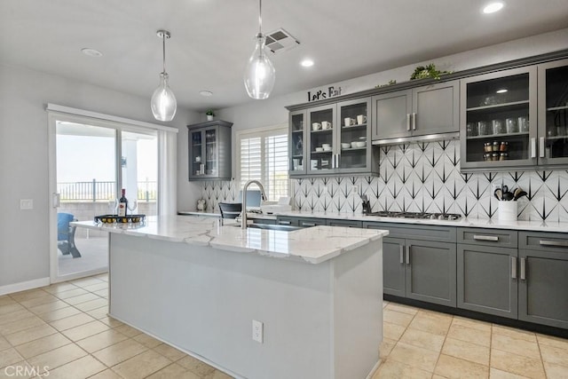 kitchen featuring sink, hanging light fixtures, stainless steel gas cooktop, a kitchen island with sink, and light stone counters