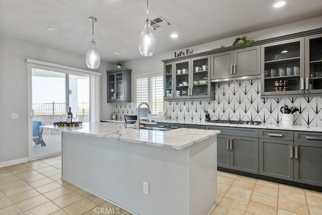 kitchen featuring a center island with sink, visible vents, light stone counters, stainless steel gas cooktop, and a sink