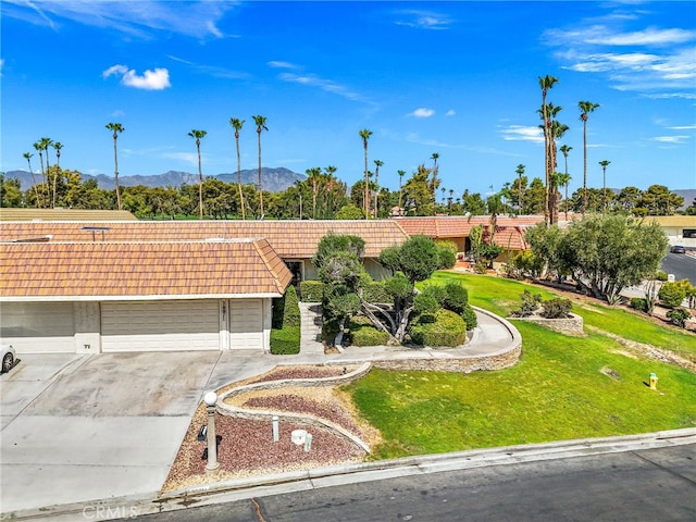 view of front facade featuring a front lawn, a mountain view, a tiled roof, concrete driveway, and an attached garage