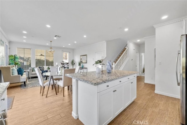 kitchen with light stone countertops, white cabinets, a kitchen island, decorative light fixtures, and stainless steel fridge