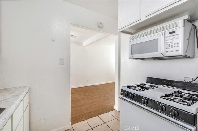 kitchen with light tile patterned floors, white cabinetry, light stone counters, and white appliances