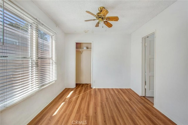 unfurnished bedroom with ceiling fan, a closet, a textured ceiling, and light hardwood / wood-style floors