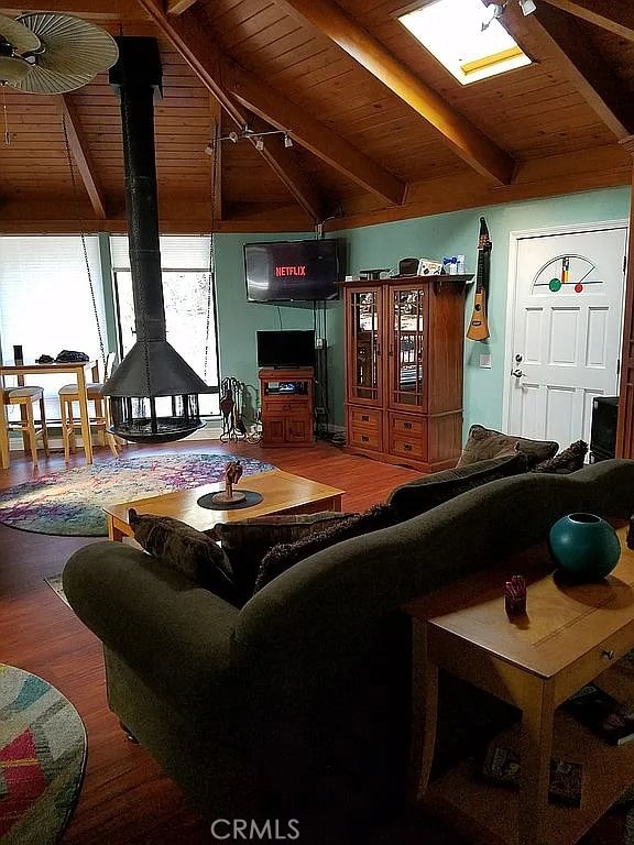 living room with vaulted ceiling with beams, wood ceiling, a wood stove, and hardwood / wood-style floors