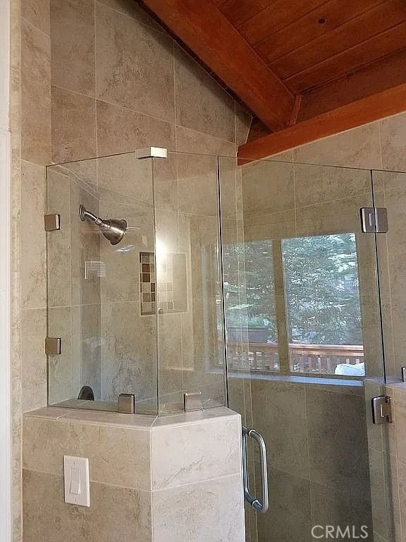 bathroom with a shower with shower door, vaulted ceiling with beams, and wood ceiling