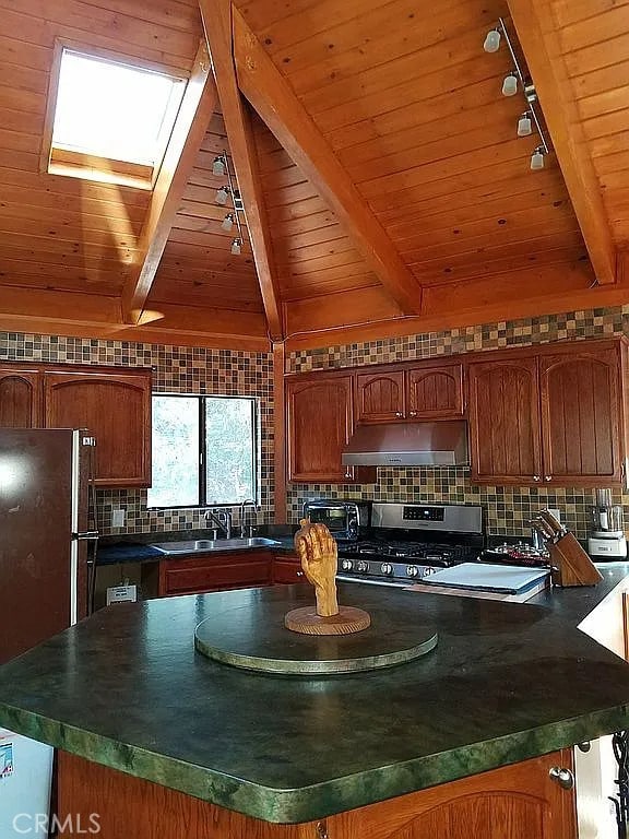 kitchen featuring vaulted ceiling with skylight, a center island, sink, stainless steel range with gas cooktop, and wood ceiling