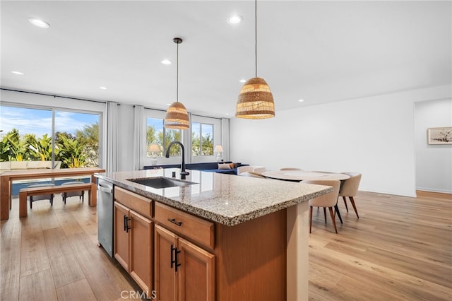 kitchen featuring sink, hanging light fixtures, light hardwood / wood-style flooring, an island with sink, and light stone countertops