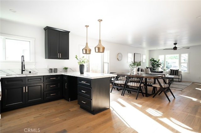 kitchen featuring kitchen peninsula, sink, light hardwood / wood-style flooring, and decorative light fixtures