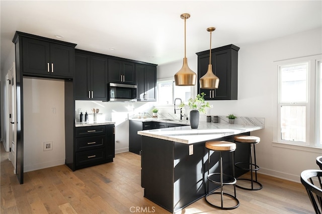 kitchen with kitchen peninsula, decorative light fixtures, a kitchen breakfast bar, light wood-type flooring, and sink