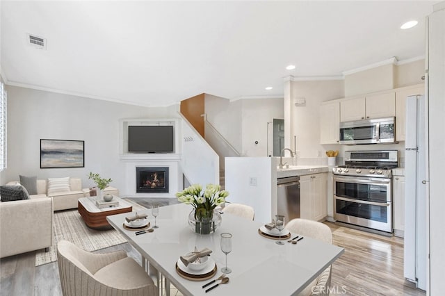 dining area with sink, crown molding, and light wood-type flooring