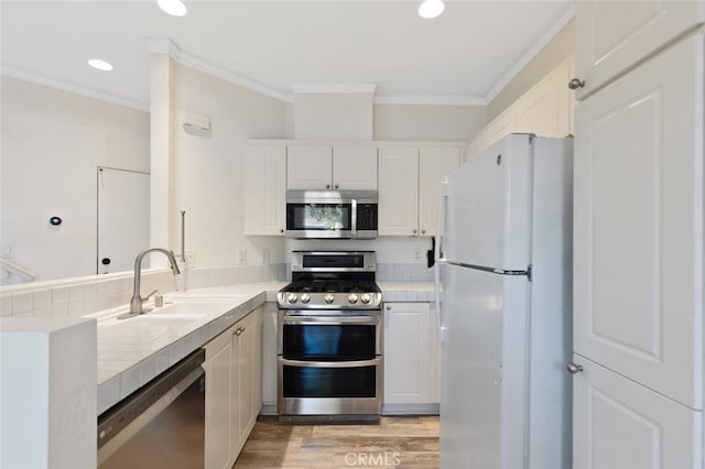 kitchen with light hardwood / wood-style floors, sink, white cabinetry, ornamental molding, and stainless steel appliances