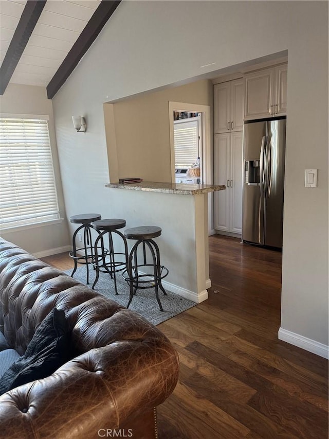 kitchen with light stone countertops, dark hardwood / wood-style flooring, stainless steel fridge with ice dispenser, kitchen peninsula, and lofted ceiling with beams